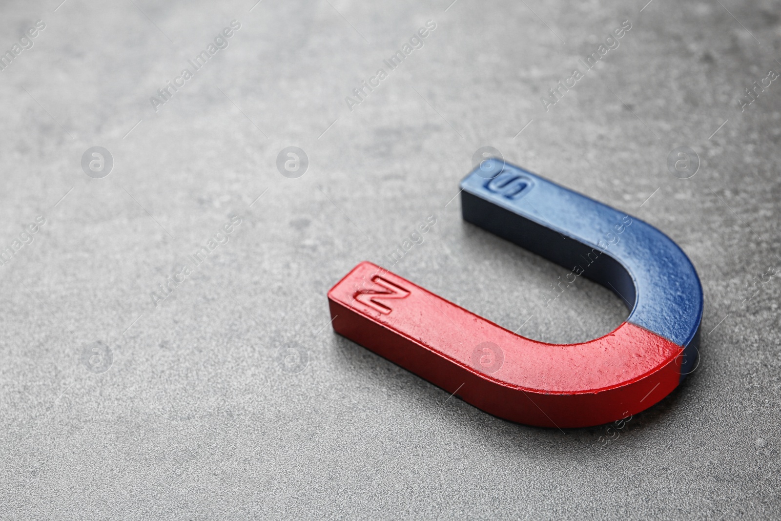 Photo of Red and blue horseshoe magnet on grey background. Space for text