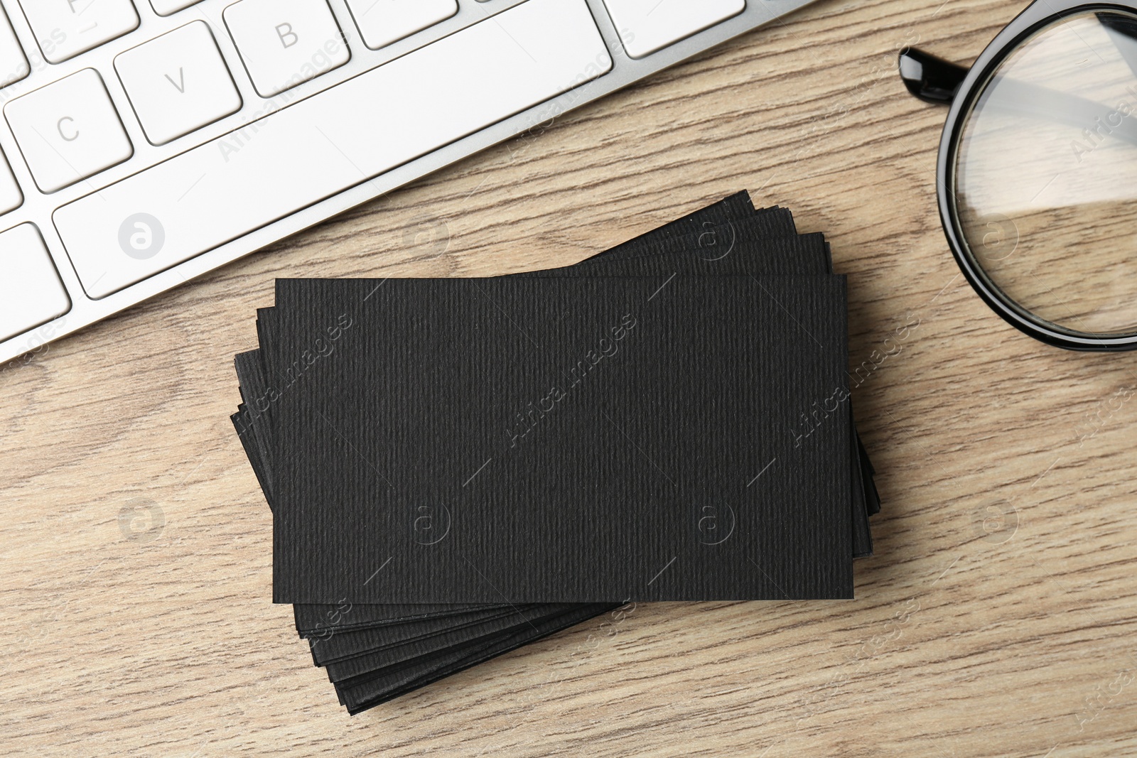 Photo of Blank black business cards, computer keyboard and glasses on wooden table, flat lay. Mockup for design