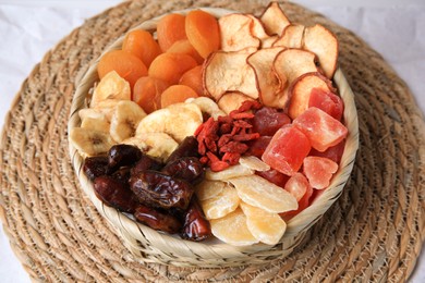 Photo of Wicker basket with different dried fruit on mat