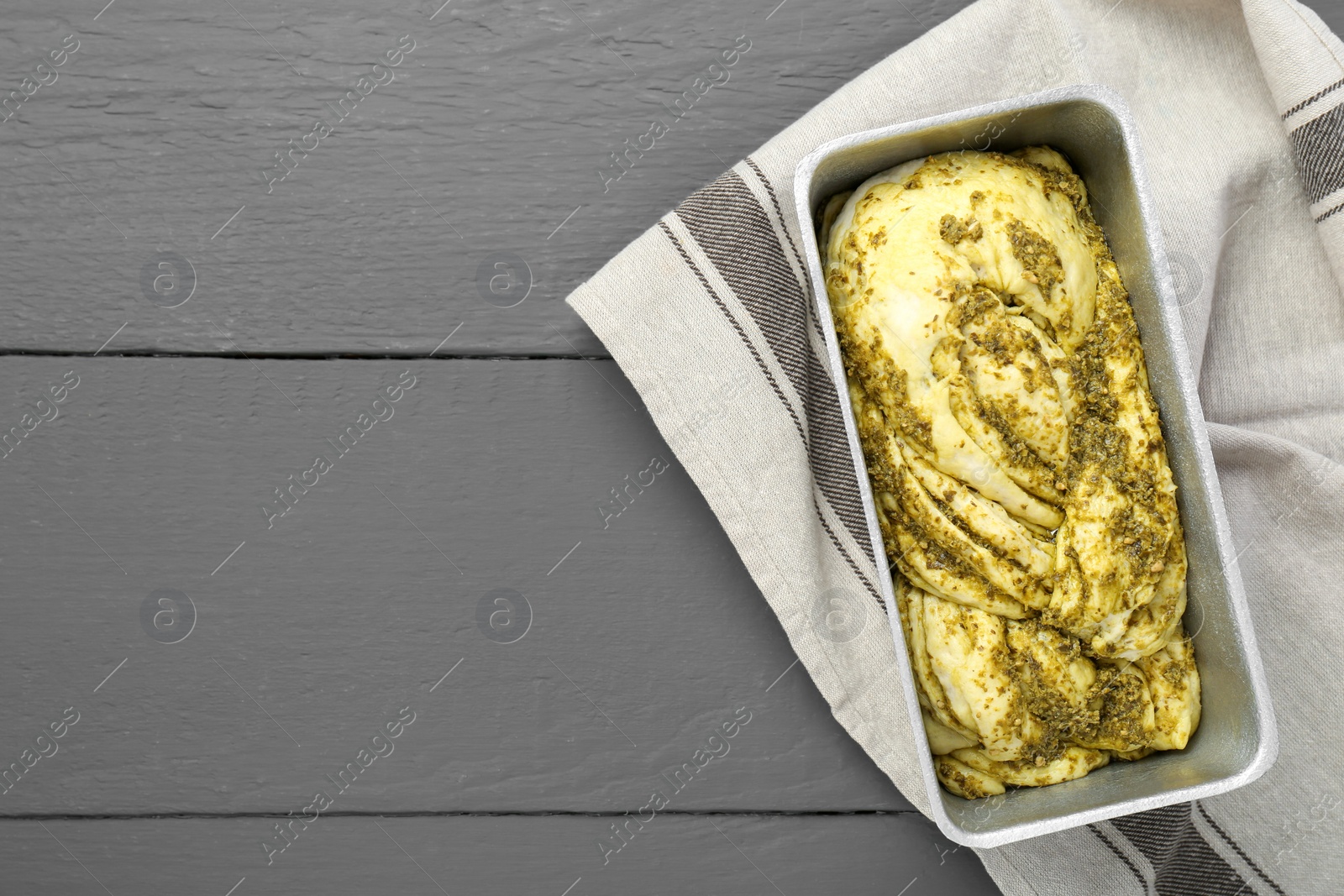 Photo of Uncooked pesto bread in baking dish on grey wooden table, top view. Space for text