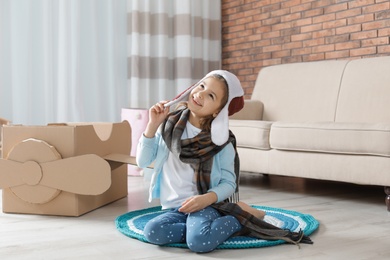 Photo of Cute little girl playing with cardboard airplane in living room