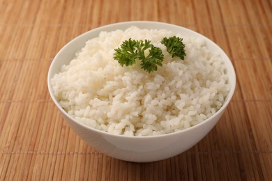 Photo of Bowl with delicious rice and parsley on bamboo mat