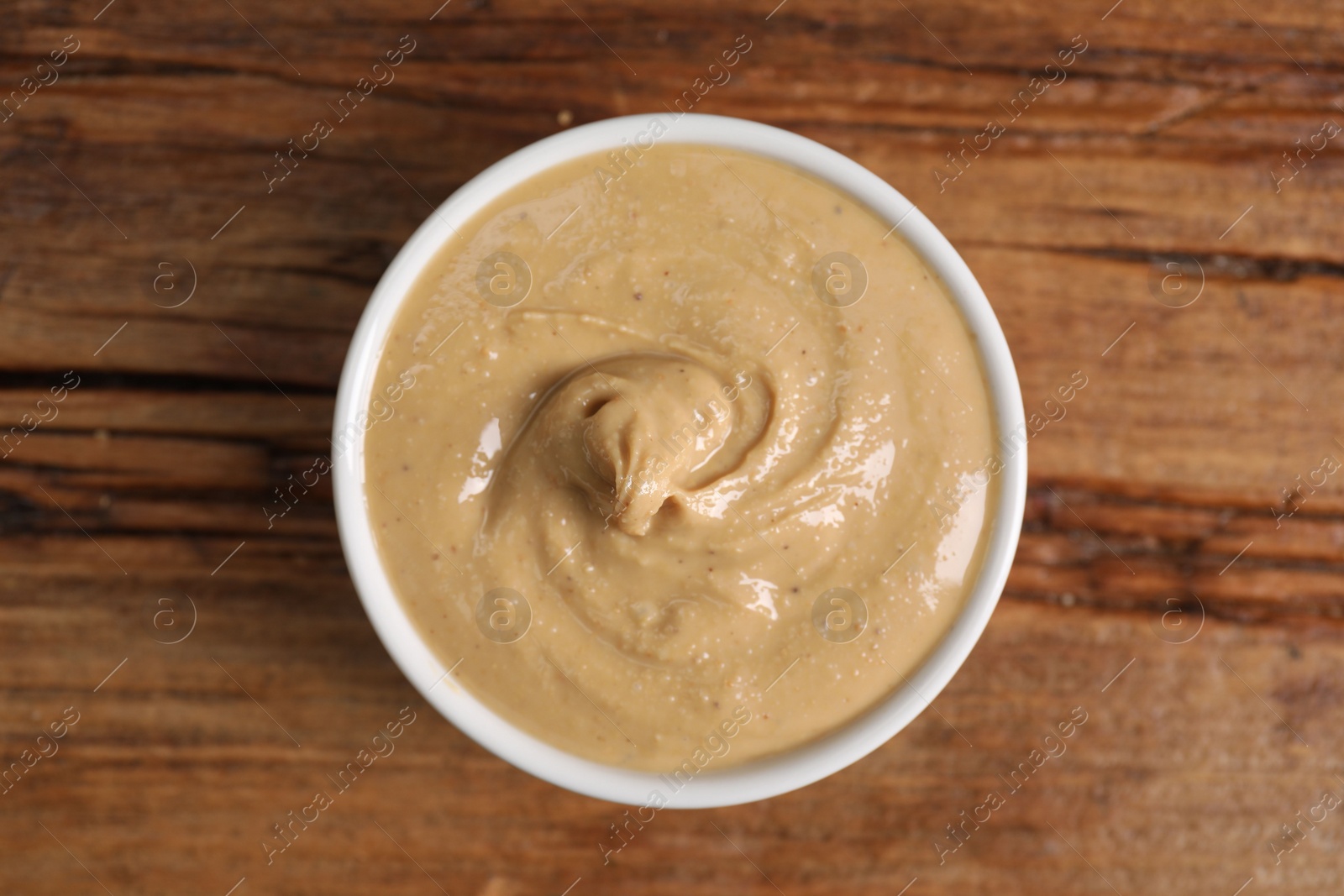 Photo of Delicious nut butter in bowl on wooden table, top view