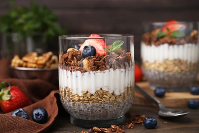 Photo of Tasty granola with berries, yogurt and chia seeds in glass on wooden table, closeup