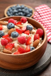 Photo of Tasty oatmeal porridge with berries and almond nuts in bowl served on table, closeup