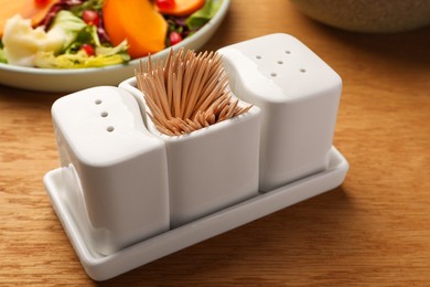 Photo of Holder with salt, pepper and toothpicks on wooden table, closeup