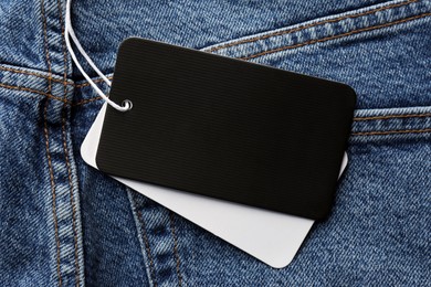 Photo of Cardboard tags with space for text on blue jeans, top view