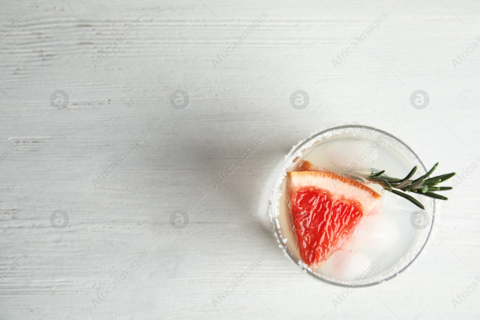 Photo of Glass of grapefruit cocktail on wooden table, top view. Space for text