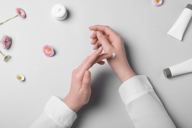 Young woman with perfect smooth skin applying hand cream on light background, top view