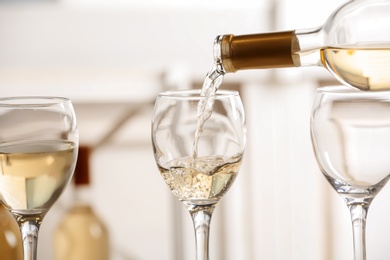 Photo of Pouring delicious white wine into glass on light background