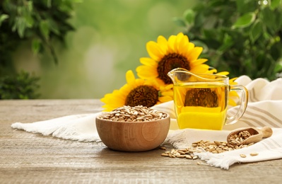 Photo of Sunflower oil and seeds on wooden table against blurred background, space for text