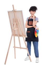 Young woman holding brush and artist`s palette near easel with canvas against white background