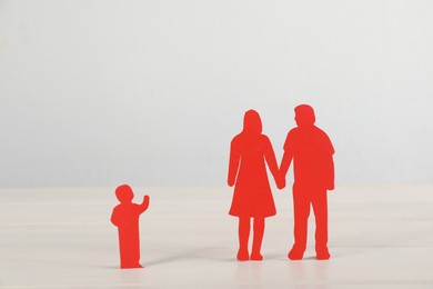 Photo of Paper figures of couple and lonely kid on white table. Child adoption concept