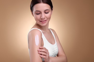 Beautiful woman with smear of body cream on her shoulder against light brown background