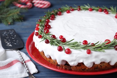 Traditional Christmas cake decorated with rosemary and cranberries on blue wooden table, closeup