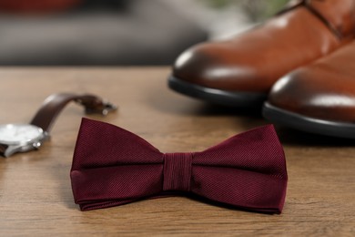 Photo of Stylish burgundy bow tie, wristwatch and shoes on wooden table, closeup