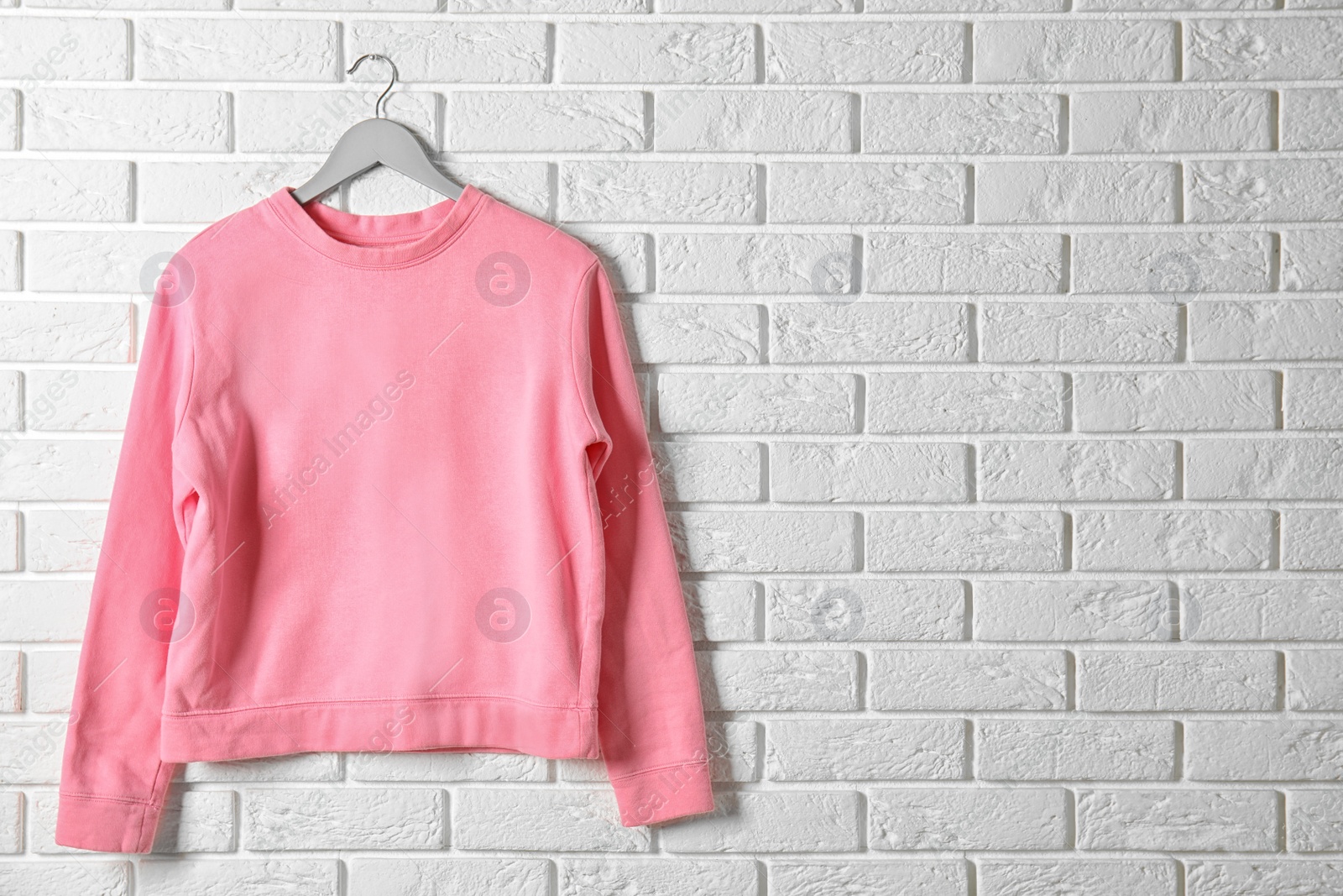 Photo of Hanger with pink sweatshirt against brick wall. Mockup for design