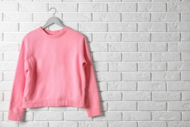 Photo of Hanger with pink sweatshirt against brick wall. Mockup for design