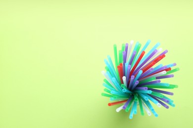 Colorful plastic drinking straws on green background, top view. Space for text