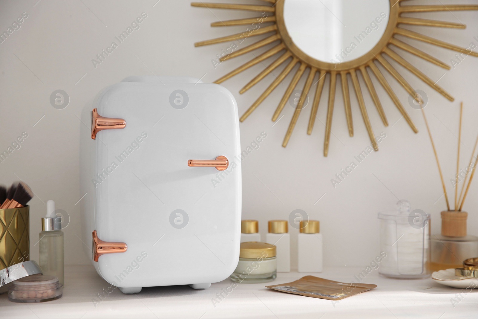 Photo of Cosmetics refrigerator and skin care products on white vanity table indoors