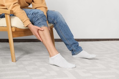 Photo of Man suffering from leg pain on armchair indoors, closeup