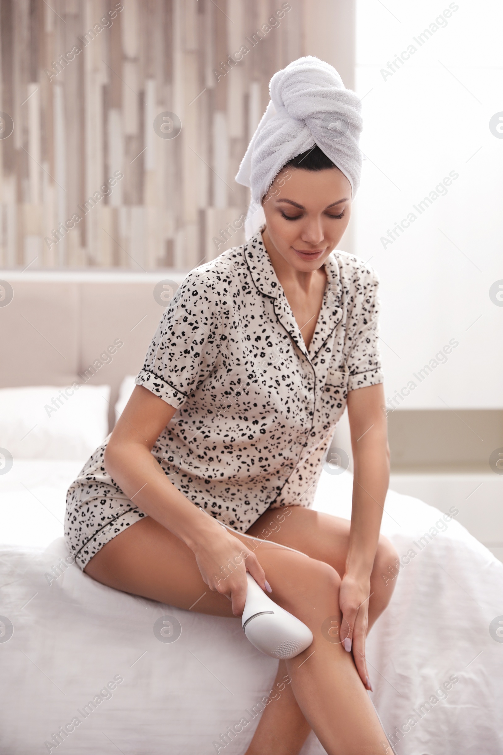 Photo of Young woman epilating her legs in bedroom