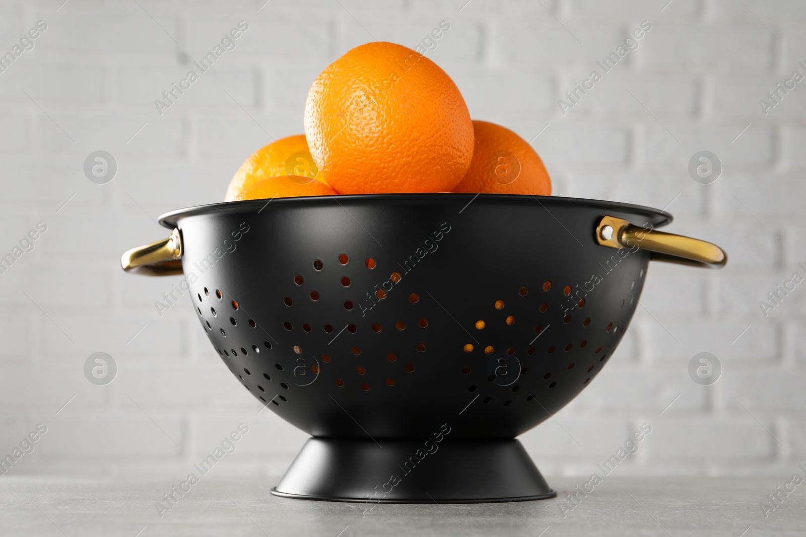 Photo of Fresh ripe oranges in black colander on light grey table