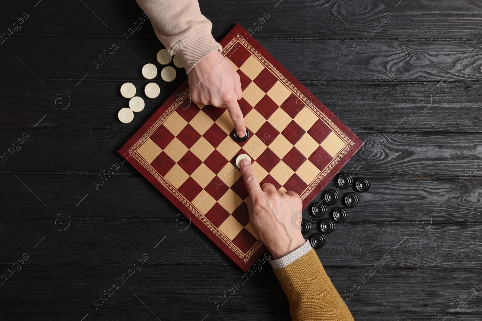 Photo of Man playing checkers with partner at black wooden table, top view
