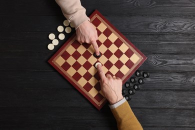 Photo of Man playing checkers with partner at black wooden table, top view
