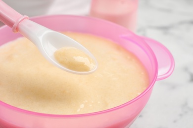 Photo of Spoon of healthy baby food over bowl on table, closeup