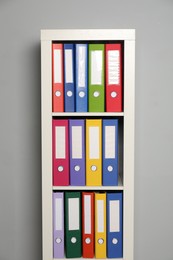 Colorful binder office folders on shelving unit near light grey wall