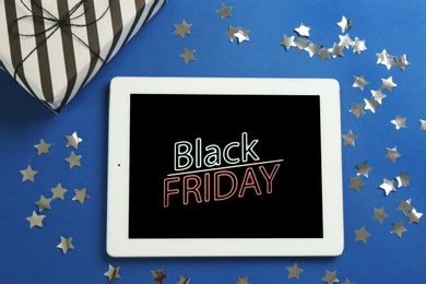 Photo of Tablet with Black Friday announcement, confetti and gift on blue background, flat lay