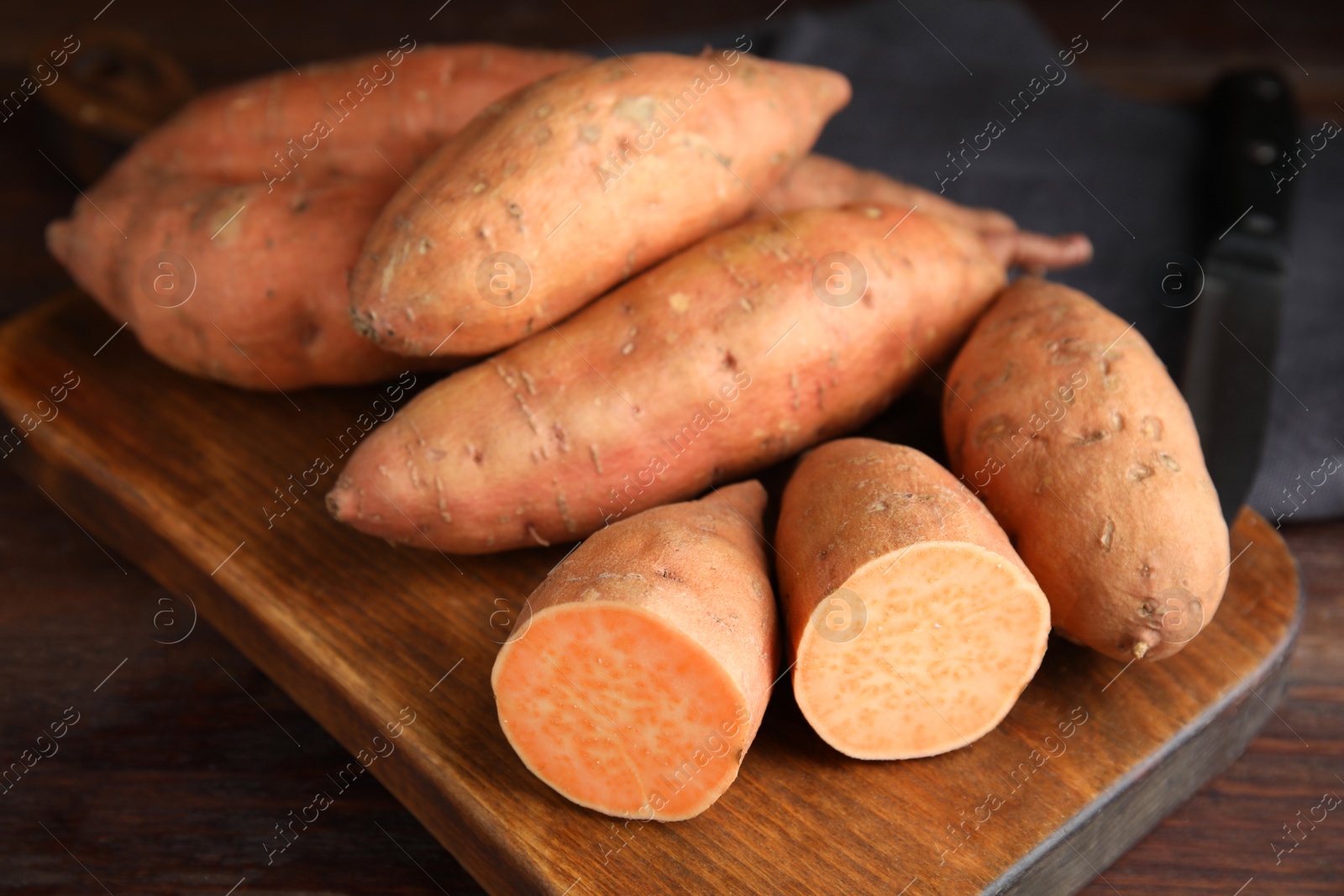 Photo of Whole and cut ripe sweet potatoes on wooden board, closeup