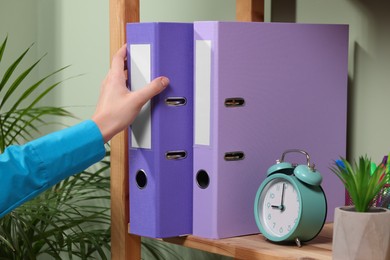 Woman taking binder office folder from shelving unit indoors, closeup