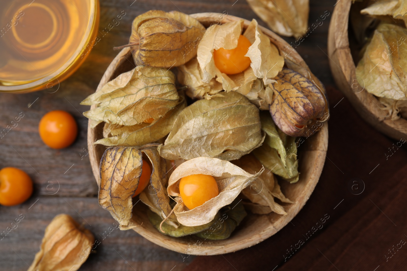 Photo of Ripe physalis fruits with calyxes in bowl on wooden table, flat lay