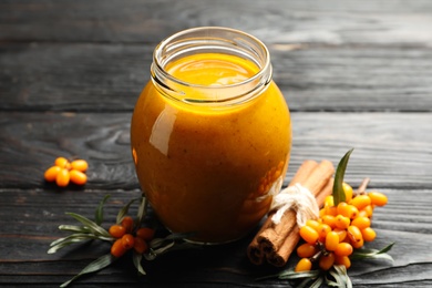 Photo of Delicious sea buckthorn jam and fresh berries on black wooden table