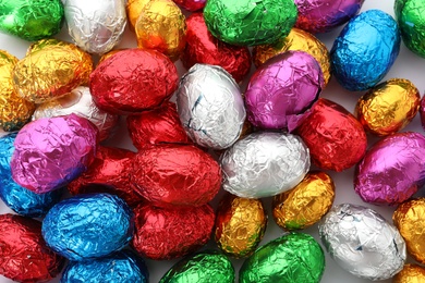 Photo of Many chocolate eggs wrapped in bright foil as background, top view