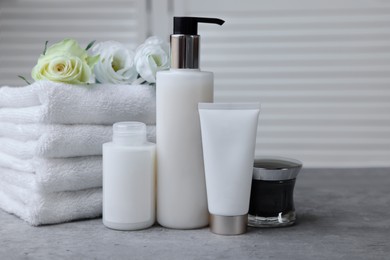 Photo of Towels, cosmetic products and flowers on grey table indoors
