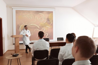 Image of Lecture in gastroenterology. Professors and doctors in conference room. Projection screen with illustration of helminths
