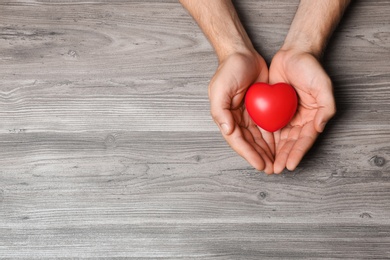 Photo of Young man holding red heart on grey wooden background, top view with space for text. Donation concept