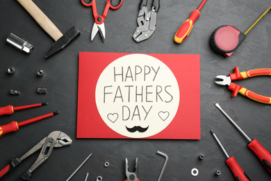 Photo of Card with phrase HAPPY FATHER'S DAY and different tools on stone background, flat lay