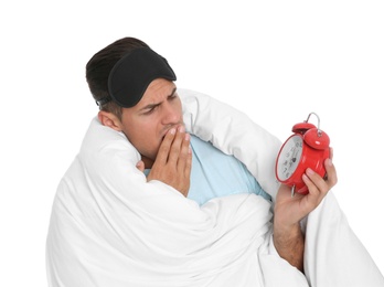 Photo of Man in sleeping mask wrapped with blanket holding alarm clock on white background