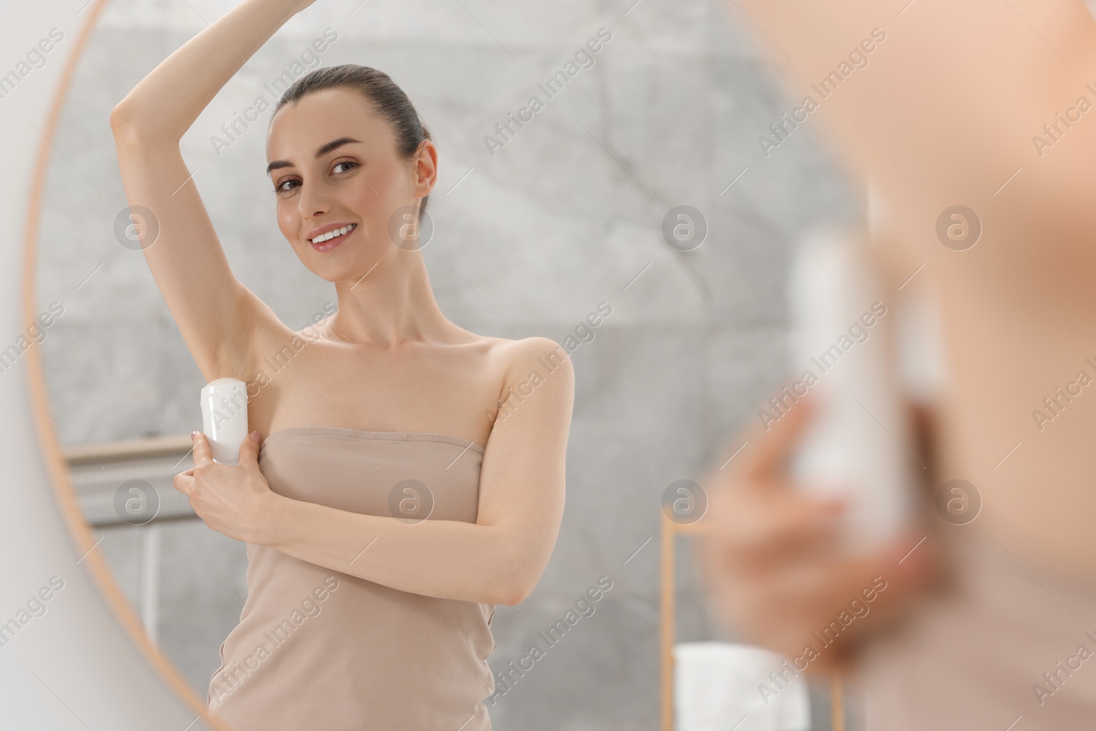 Photo of Beautiful woman applying deodorant near mirror in bathroom