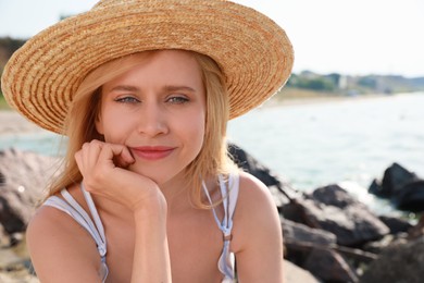 Beautiful young woman with straw hat near sea on sunny day in summer