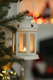 Christmas lantern with burning candle on fir tree indoors, closeup