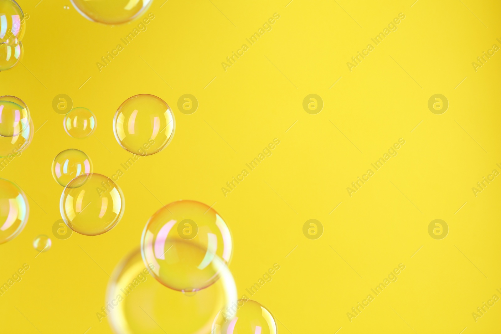 Photo of Beautiful transparent soap bubbles on yellow background, space for text