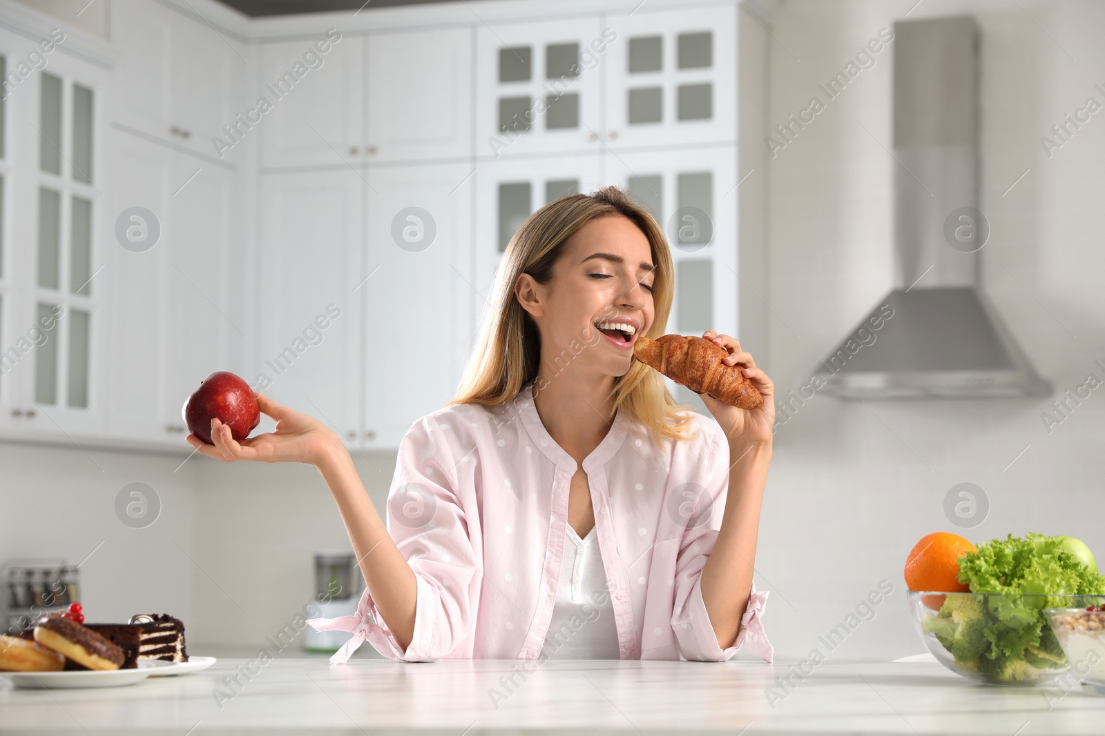 Photo of Woman choosing between sweets and healthy food at white table in kitchen