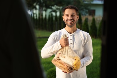 Photo of Man with net bag of products helping his senior neighbour outdoors