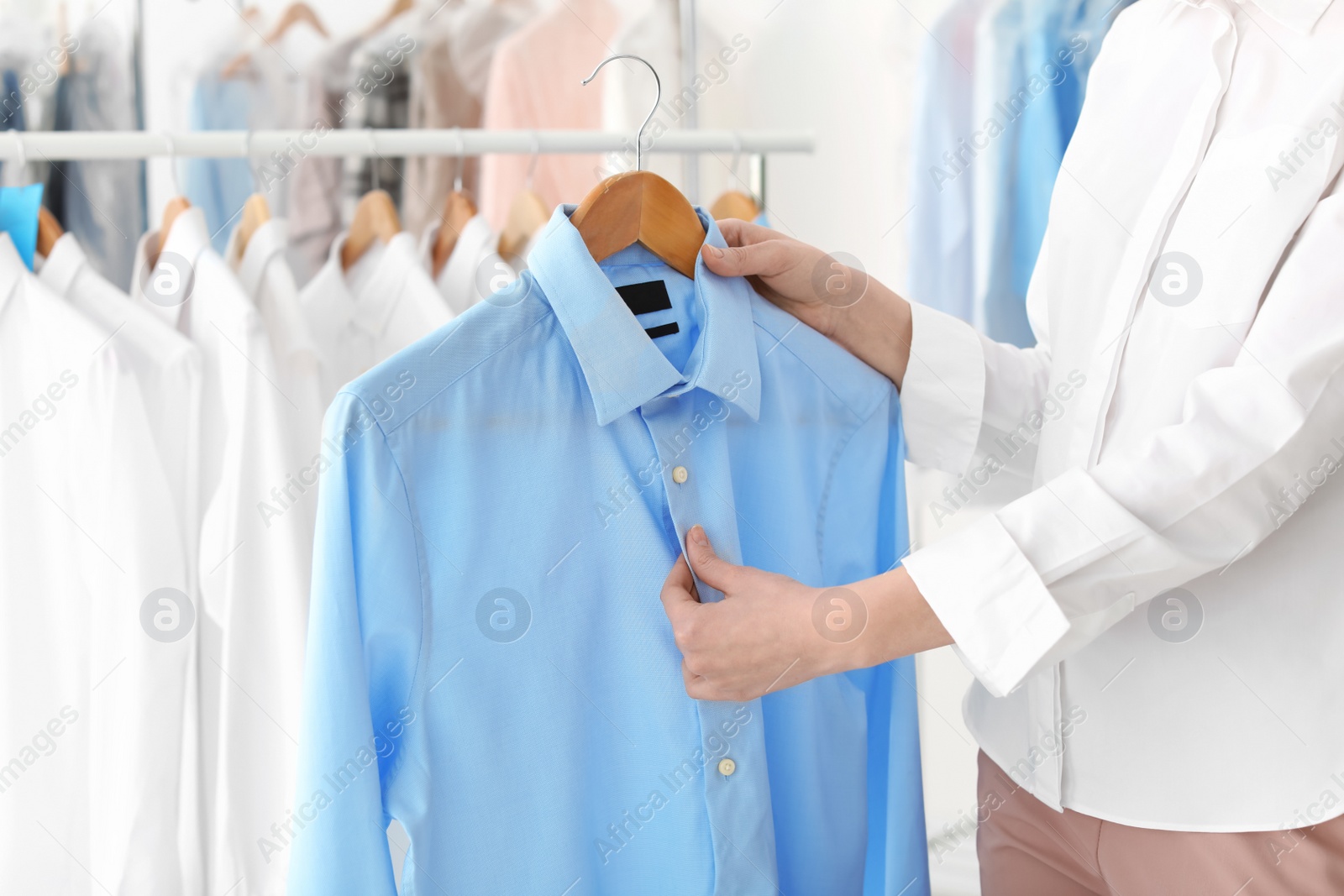 Photo of Young woman holding hanger with shirt at dry-cleaner's