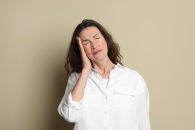Mature woman suffering from headache on beige background